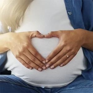 Pregnant individual forming a heart shape over the belly, symbolizing prenatal care.